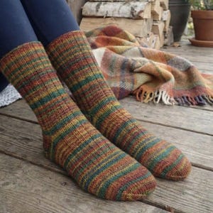 May include: A pair of colorful knitted socks with horizontal stripes in shades of orange, green, and brown. The socks are worn on legs with blue pants. A plaid blanket with fringe is in the background.
