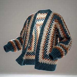 以下が含まれることがあります： 手作りの、開いたフロントのグラニースクエアパターンのクロシェカーディガン。セーターは、ティール、クリーム、ラストカラーの糸を使ったカラーブロックデザインが特徴です。袖とトリムは無地のティールカラーです。カーディガンは居心地の良い、ボヘミアンスタイルです。