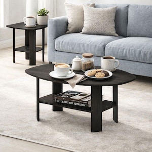 May include: A dark brown oval coffee table with a lower shelf, holding books. A white coffee cup and saucer, a plate of cookies, and a sugar bowl are on the table. A matching side table and a light blue sofa are in the background.
