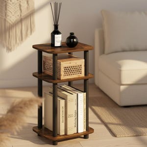 May include: A three-tiered, dark brown side table with black metal supports. The top shelf holds a black diffuser bottle and a small black vase. The middle shelf has a wooden crate, and the bottom shelf displays books. The table is in a living room setting.