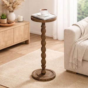 May include: A small, round, wooden side table with a dark brown finish. The table has a turned, beaded column and a circular base. A book and a cup of coffee sit on top. The table is approximately 28 inches tall.