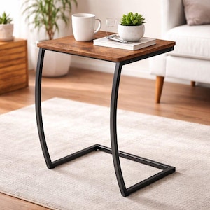 May include: A small, brown side table with a square top and a black metal frame. The table has a curved leg design and is holding a white mug, a small glass, a book, and a potted succulent.
