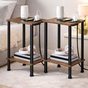 May include: Two side tables with a dark brown wood-look top and a lower shelf. The tables have black metal legs. Each table has a white speaker, a phone, and a charging block on top. Headphones and books are on the lower shelf.