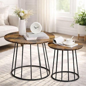 May include: Two round coffee tables with a rustic wood-look top and black metal legs. The larger table has a vase with flowers, a clock, and books. The smaller table has a cup and saucer.