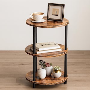 May include: A three-tiered side table with a distressed wood finish and black metal supports. The top shelf holds a framed picture and a cup of coffee. The middle shelf has books and glasses, and the bottom shelf displays small potted plants.
