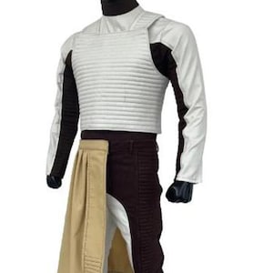 May include: A costume featuring a white, padded vest over a black turtleneck and white sleeves. The outfit includes brown pants with a tan panel and a matching tan skirt-like piece. Black gloves complete the look.