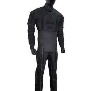 Pu&ograve; includere: Tuta tattica nera con cuciture bianche, esposta su un manichino. La tuta comprende un top a maniche lunghe, pantaloni e un giubbotto protettivo. Il manichino ha testa e mani nere.