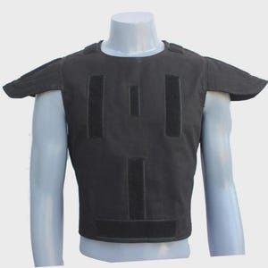 Peut inclure: Un gilet tactique noir avec des épaulettes et plusieurs panneaux Velcro. Le gilet est présenté sur un mannequin, mettant en valeur son design et ses caractéristiques. Le gilet est conçu pour la protection et est probablement utilisé dans les forces de l'ordre ou l'armée.