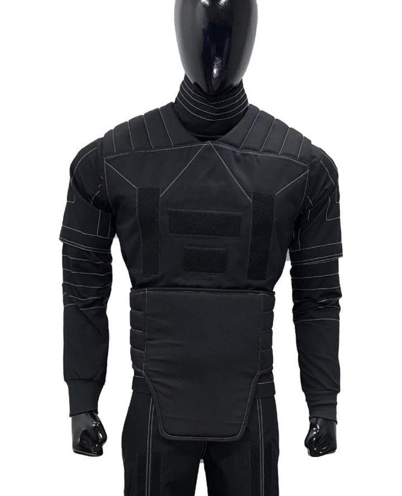 Pu&ograve; includere: Gilet tattico nero con maniche lunghe, esposto su un manichino. Il gilet presenta diversi pannelli con cuciture bianche e chiusure a strappo. Il manichino indossa un dolcevita e guanti neri.