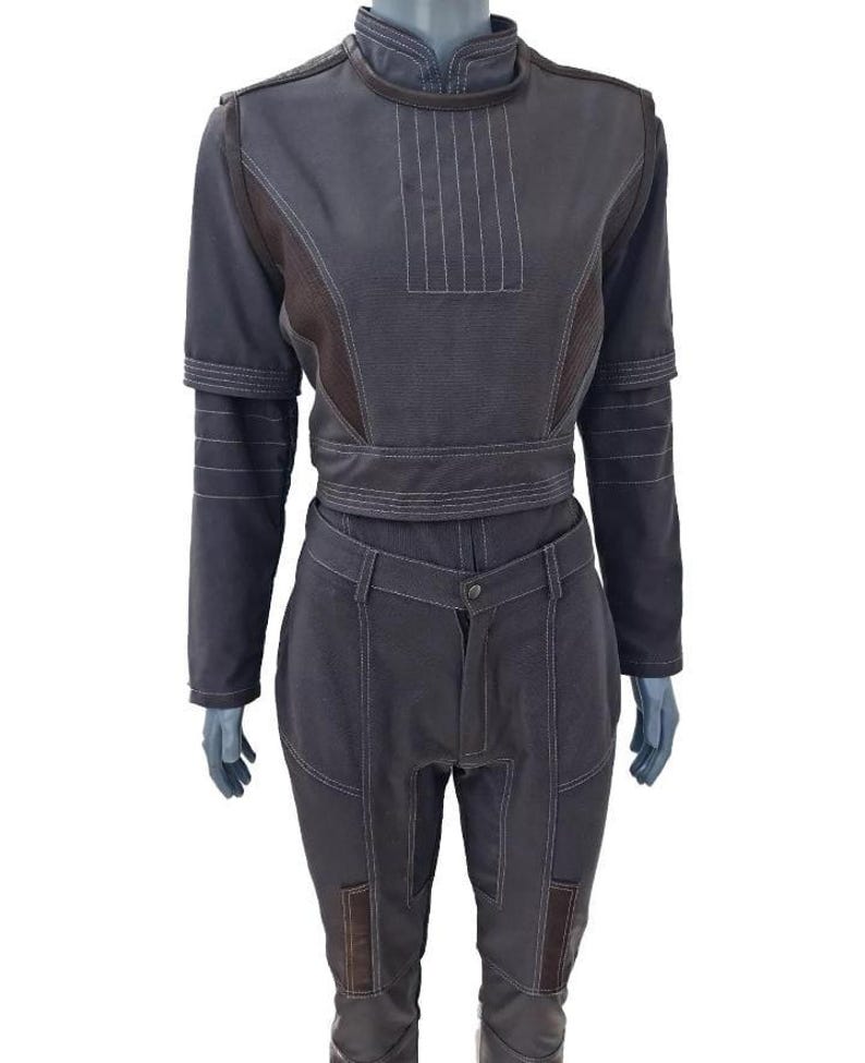 K&ouml;nnte beinhalten: Ein zweiteiliges Outfit in Dunkelgrau mit wei&szlig;en Nahtdetails. Das Oberteil hat einen hohen Kragen und lange &Auml;rmel, und die Hose ist hoch tailliert. Braune Stoffakzente erg&auml;nzen das Outfit. Das Outfit wird auf einer Schaufensterpuppe pr&auml;sentiert.