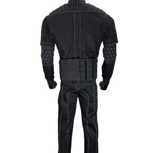 Pu&ograve; includere: Tuta tattica nera con cuciture bianche, esposta su un manichino. La tuta include una giacca con dettagli geometrici sulle maniche, una cintura con pi&ugrave; scomparti e pantaloni abbinati. Il manichino ha una testa nera.