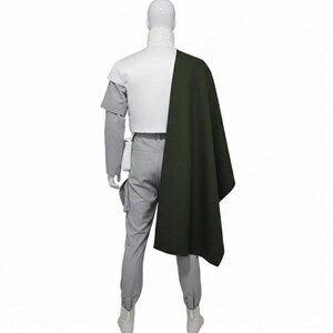 May include: A costume set featuring a white high-neck top, light grey trousers with side pockets, and a dark olive green cape draped over one shoulder. The ensemble is displayed on a mannequin, showcasing a structured design with layered elements.