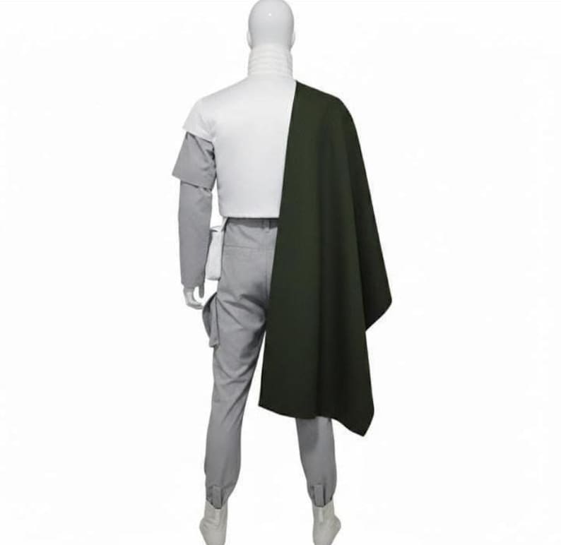 May include: A costume set featuring a white high-neck top, light grey trousers with side pockets, and a dark olive green cape draped over one shoulder. The ensemble is displayed on a mannequin, showcasing a structured design with layered elements.