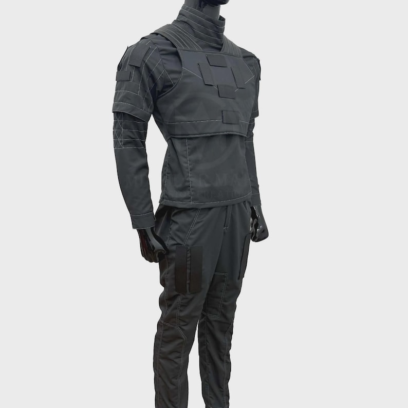May include: A dark gray tactical uniform consisting of a long-sleeved shirt with a high collar and a structured chest plate featuring rectangular panels. The matching trousers include reinforced thigh sections and visible stitching throughout the garment.