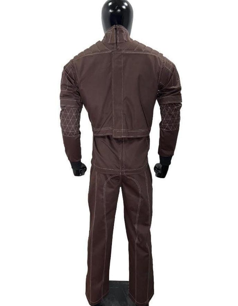 Puede incluir: Traje protector marr&oacute;n con costuras blancas, exhibido en un maniqu&iacute;. La chaqueta tiene paneles acolchados en los hombros y la parte superior de la espalda, con coderas con dise&ntilde;os geom&eacute;tricos. El pantal&oacute;n es de corte recto. El traje est&aacute; dise&ntilde;ado para protecci&oacute;n.