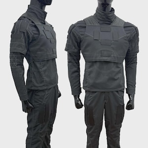 May include: A black tactical uniform set consisting of a long-sleeved shirt with a high collar, a chest plate with rectangular patches, and matching trousers. The garment features reinforced stitching, shoulder panels, and rectangular leg pockets.