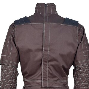 May include: A dark brown jacket featuring a high collar with a back zipper, dark shoulder epaulets, and white contrast stitching. The sleeves display a geometric triangular quilted pattern, while the back panel includes a vertical central seam.