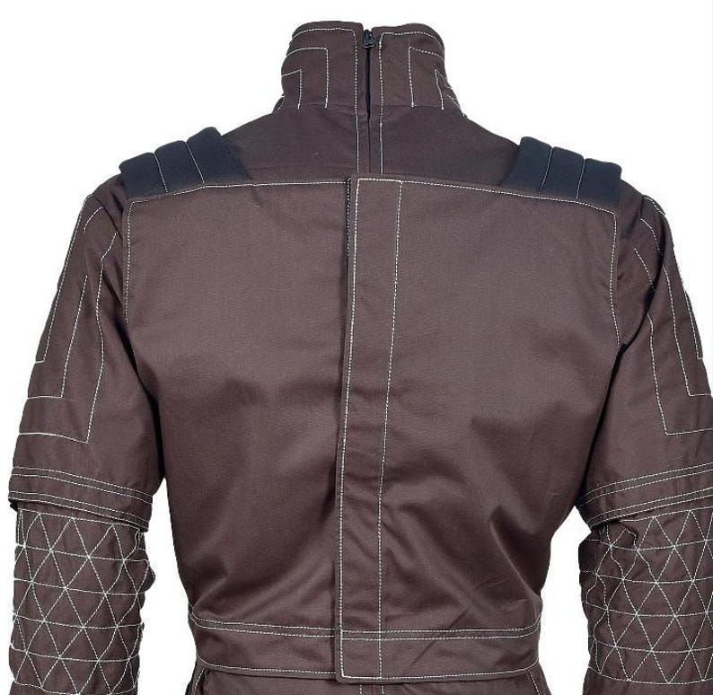 May include: A dark brown jacket featuring a high collar with a back zipper, dark shoulder epaulets, and white contrast stitching. The sleeves display a geometric triangular quilted pattern, while the back panel includes a vertical central seam.