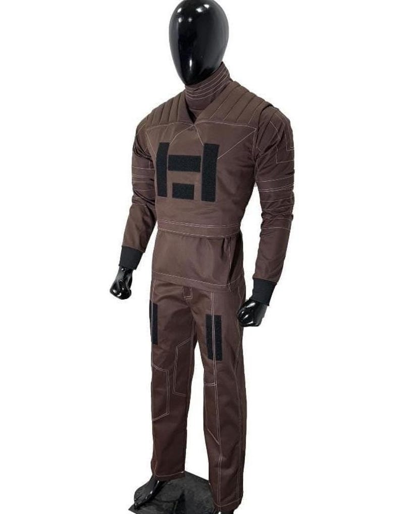 Puede incluir: Mono marr&oacute;n con cuello alto y mangas largas, exhibido en un maniqu&iacute;. El traje presenta un gran dise&ntilde;o rectangular negro en el pecho y detalles negros en las mangas y las piernas. Costuras blancas.