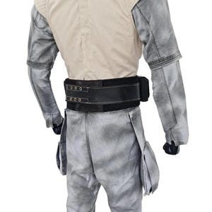 May include: A costume featuring a light tan vest with shoulder pads, gray sleeves, and matching pants. A wide black belt with silver buckles and a pouch detail the waist. The outfit is designed with a weathered, textured appearance.