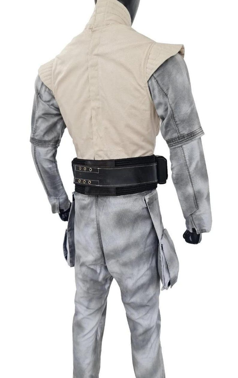 May include: A costume featuring a light tan vest with shoulder pads, gray sleeves, and matching pants. A wide black belt with silver buckles and a pouch detail the waist. The outfit is designed with a weathered, textured appearance.