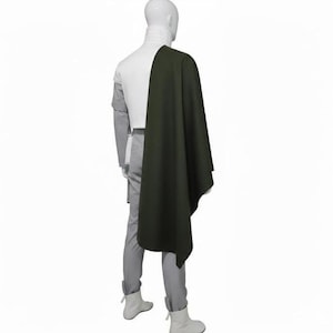 May include: A white high-neck top paired with light grey trousers and white boots, featuring a long, dark olive green cape draped over the right shoulder. The ensemble is displayed on a mannequin, showcasing a layered design with a solid colour palette.