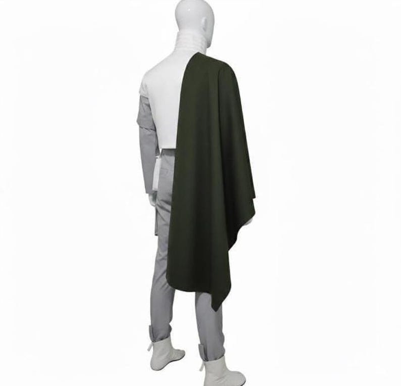 May include: A white high-neck top paired with light grey trousers and white boots, featuring a long, dark olive green cape draped over the right shoulder. The ensemble is displayed on a mannequin, showcasing a layered design with a solid colour palette.