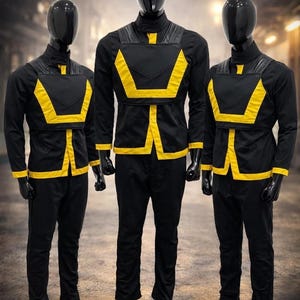 May include: Three mannequins dressed in black uniforms with yellow accents. The uniforms include long-sleeved shirts, pants, and a chest piece. The yellow detailing outlines the chest piece and runs down the front of the shirt.