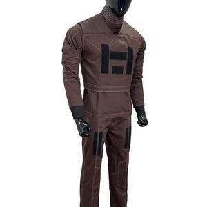 Puede incluir: Mono marr&oacute;n con detalles negros y costuras blancas. La parte superior de manga larga presenta un cuello alto y un gran dise&ntilde;o rectangular negro en el pecho. Los pantalones tienen parches rectangulares negros en las piernas. El maniqu&iacute; tiene una cabeza negra y guantes negros.