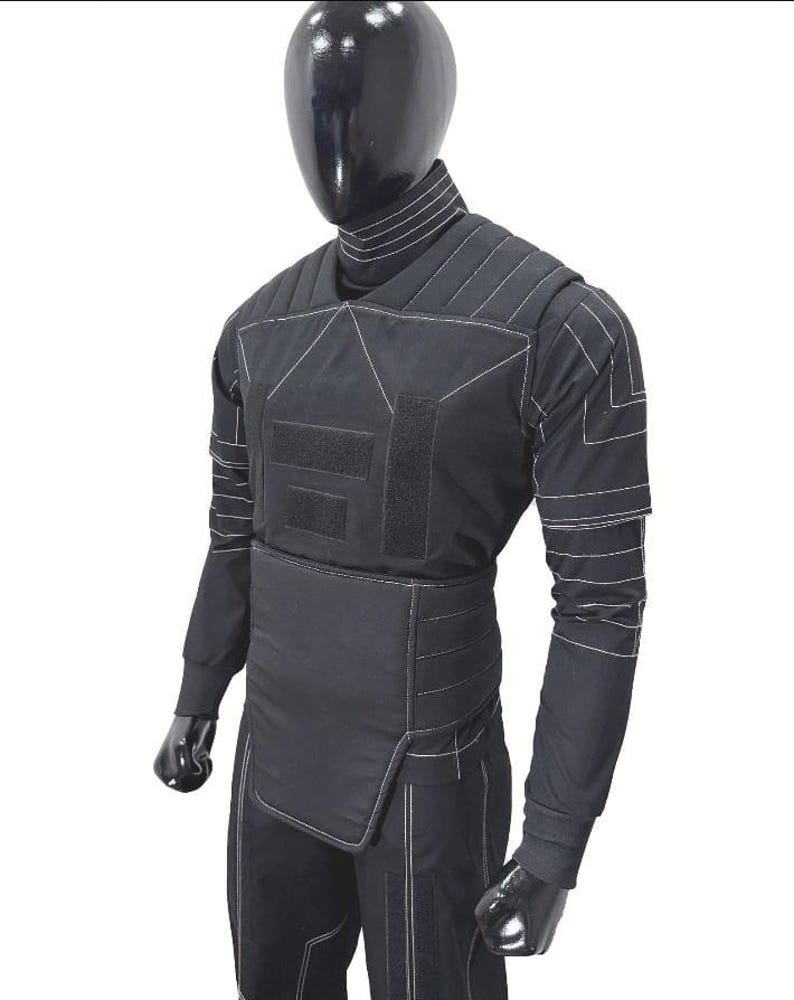 Pu&ograve; includere: Set di gilet e pantaloni tattici neri esposto su un manichino. Il gilet presenta cuciture bianche, pannelli multipli e chiusure a strappo. La camicia a maniche lunghe e i pantaloni sono anch'essi neri, con dettagli di cucitura bianchi.