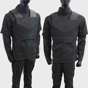 May include: Two black costumes displayed on mannequins, each featuring a high-neck long-sleeve shirt with white stitched detailing, a structured chest plate with a V-shaped seam, shoulder padding, and matching black trousers with reinforced knee panels.