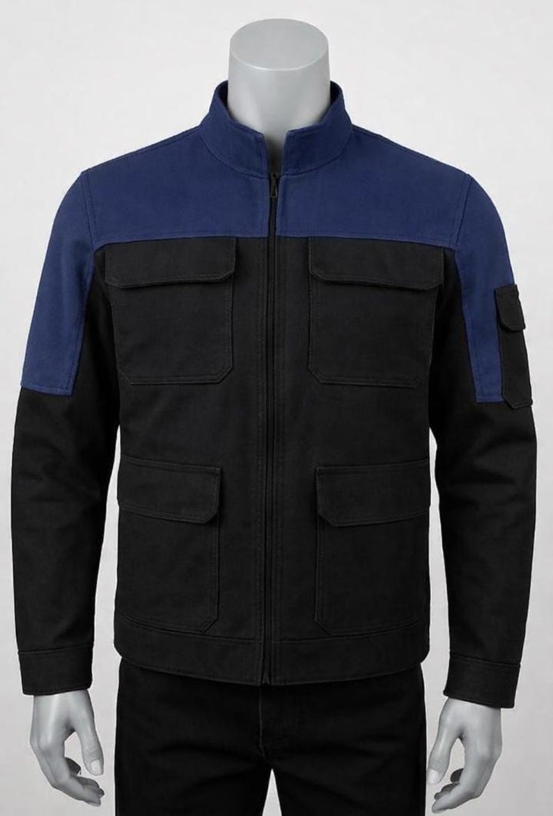 Op de afbeelding: Zwarte jas met een blauw juk en mouwen. De jas heeft een opstaande kraag, een ritssluiting over de hele lengte en vier voorzakken. Een klein zakje zit op de linkermouw. De jas wordt op een mannequin gepresenteerd.