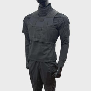 May include: A black tactical uniform set consisting of a long-sleeved shirt with a high collar, a structured chest vest with rectangular panels, and matching trousers. The ensemble features visible stitching, shoulder patches, and leg pockets.