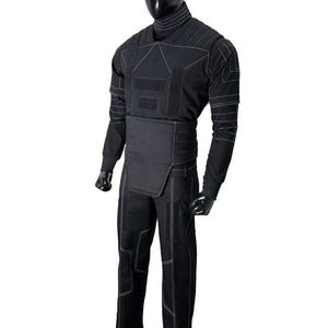 Pu&ograve; includere: Tuta tattica nera con dettagli di cuciture bianche. La tuta presenta un collo alto, maniche lunghe e un design segmentato sul petto e sulla vita. I pantaloni hanno un motivo cucito simile. Esposto su un manichino.