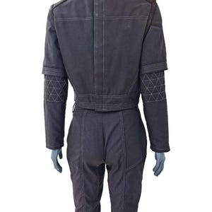 K&ouml;nnte beinhalten: Dunkelgrauer Overall mit wei&szlig;en N&auml;hten. Die Jacke hat einen kurzen Schnitt, einen braunen Kragen und geometrische Akzente an den &Auml;rmeln. Die Hose hat eine figurbetonte Silhouette.