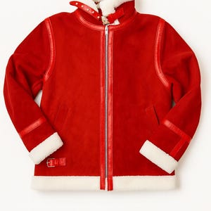 May include: A red suede jacket with a white shearling collar and cuffs. The jacket features a zip-up front, leather trim, and a buckled collar strap. The sleeves have buckled cuffs and a small pocket on the chest.
