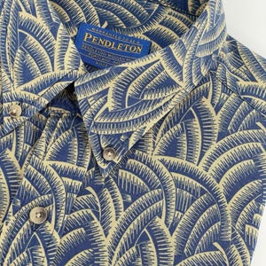 Op de afbeelding: Close-up van een blauw overhemd met knopen en een crèmekleurig, waaiervormig patroon. Het overhemd heeft een button-down kraag en een Pendleton label. De stof is een geweven materiaal. Het overhemd is een casual kledingstuk.