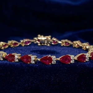 May include: A gold bracelet featuring a series of pear-shaped red gemstones alternating with small clear stones. The links are connected in a continuous circular design with a secure metal clasp visible at the back of the jewelry piece.