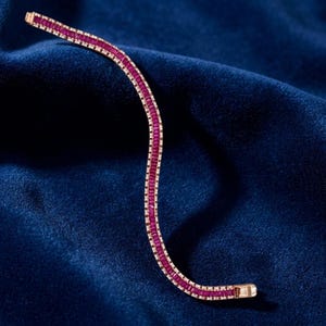 Op de afbeelding: Een flexibele armband met een doorlopende rij rechthoekige, dieprode baguette-geslepen stenen in een metalen zetting. Het ontwerp volgt een zachte, golvende lijn en toont een gelijkmatige rangschikking van levendige rode edelstenen.