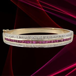 May include: A gold bangle bracelet with a row of square-cut rubies in the center, framed by two rows of small diamonds. The bracelet has a clasp closure and a polished finish. The background is a dark red and black gradient.