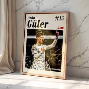 May include: Framed poster featuring soccer player Arda Güler in a white jersey, with the number 15. The poster includes the player's name, a signature, and the Turkish flag. The image is set against a light background.