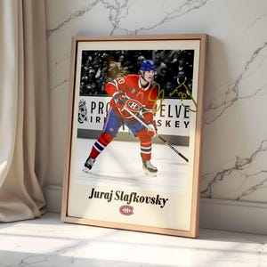 Könnte beinhalten: Gerahmter Druck mit Juraj Slafkovsky im Trikot der Montreal Canadiens. Das Bild zeigt Slafkovsky auf dem Eis mit einem Hockeyschläger, vor dem Hintergrund einer Menschenmenge. Der Druck enthält den Namen des Spielers und das Teamlogo, in einem Holzrahmen.