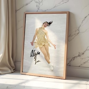 Op de afbeelding: Een ingelijste print met een kunstschaatser in een gouden kostuum, midden in een optreden op een ijsbaan. De print is gesigneerd met de naam "Alysa" in zwarte inkt. De lijst is lichtbruin en de achtergrond is een marmeren muur.