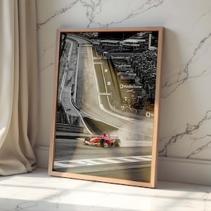 Puede incluir: Impresión enmarcada de un coche de carreras de Fórmula 1 en una pista. La imagen es mayoritariamente en blanco y negro, con el coche de carreras rojo como punto focal. La impresión está en un marco de madera marrón claro, apoyada contra una pared de mármol blanco.