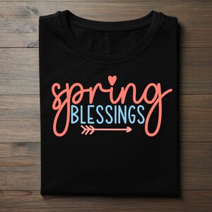 Peut inclure: T-shirt noir avec l'inscription "spring BLESSINGS" en lettres corail et bleu clair. Un petit cœur corail est au-dessus de "spring", et une flèche pointe vers la droite en dessous de "BLESSINGS".