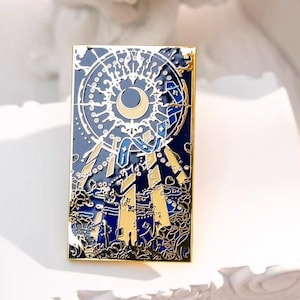Puede incluir: Pin rectangular de esmalte con borde dorado. El pin presenta un diseño celestial con una luna creciente, estrellas y formas geométricas en tonos azul, dorado y blanco. Probablemente es un accesorio decorativo.