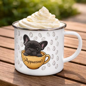 Puede incluir: Taza de esmalte blanco con una ilustración de un cachorro de bulldog francés negro en una taza de café amarilla, llena de crema batida. La taza tiene la palabra "Puppuccino?" e ilustraciones de granos de café.