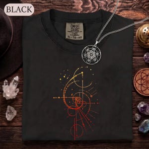 May include: A black t-shirt featuring a graphic of a golden ratio spiral composed of dots and lines in shades of yellow, orange, and red. The shirt has a Comfort Colors label and is paired with a silver-toned circular pendant necklace.