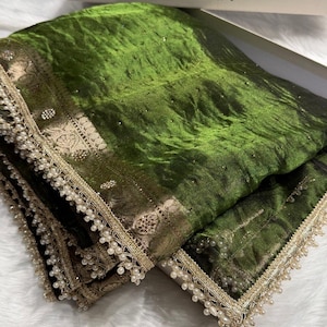 Puede incluir: Una tela de terciopelo verde intenso con un borde metálico dorado ancho y ornamentado con patrones tejidos intrincados. Los bordes están terminados con un delicado fleco de pequeñas perlas blancas. Una caja blanca con el texto ZAIRA es visible arriba.