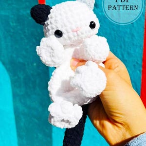 Może przedstawiać: Ręcznie robiona biało-czarna szydełkowa zabawka w kształcie kota z czarnymi oczami i różowym nosem. Kot ma czarny ogon i czarną plamę na jednym uchu. Obraz zawiera tekst "PDF PATTERN".